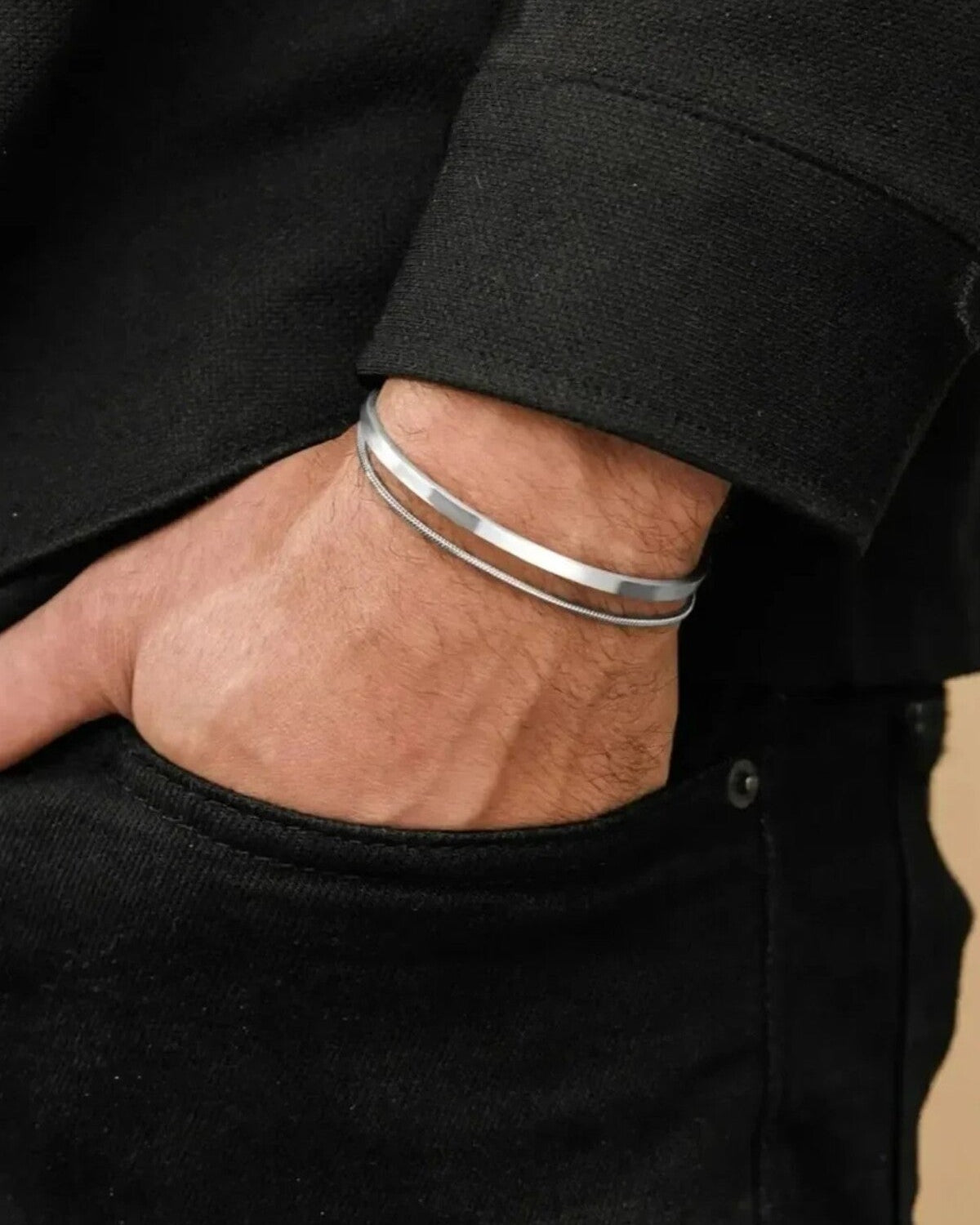 Close-up of a person wearing two silver bracelets on a black background