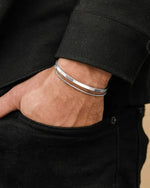 Close-up of a person wearing two silver bracelets on a black background